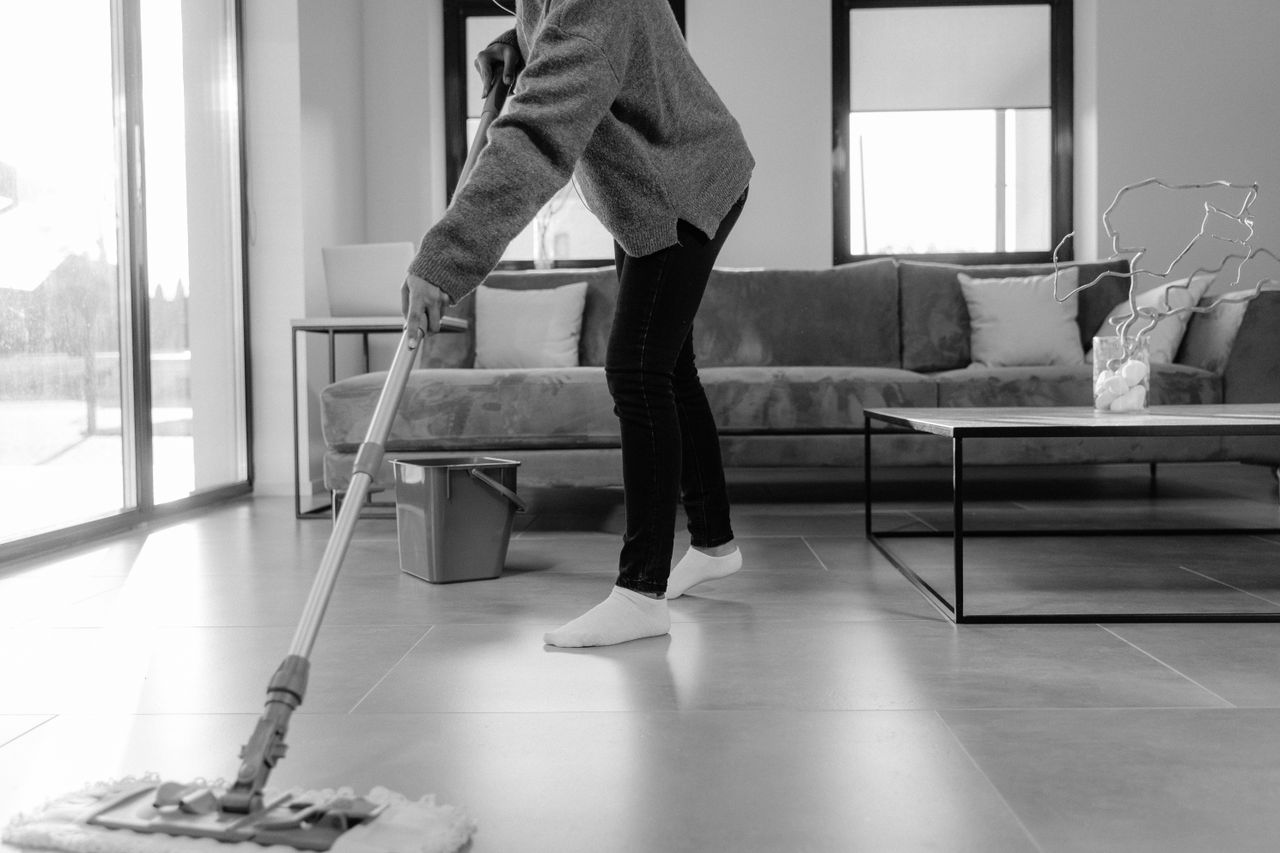 Une photo en niveaux de gris d’une personne en train de laver le sol dans un salon moderne.
